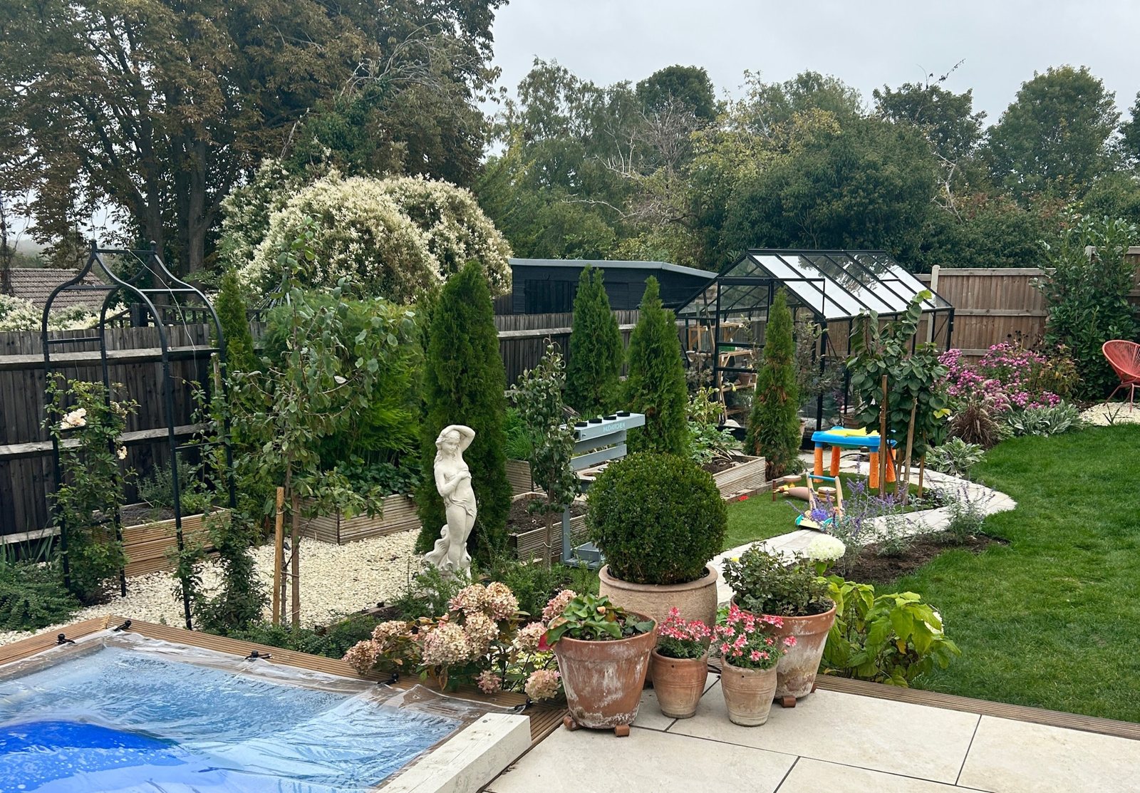 A finished garden with raised vegetable beds, tall evergreens and a greenhouse