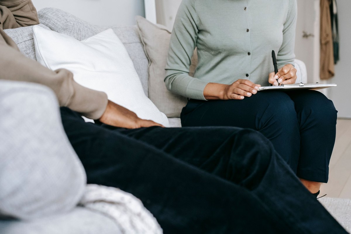 A designer taking notes on a clipboard while talking with a client on a sofa